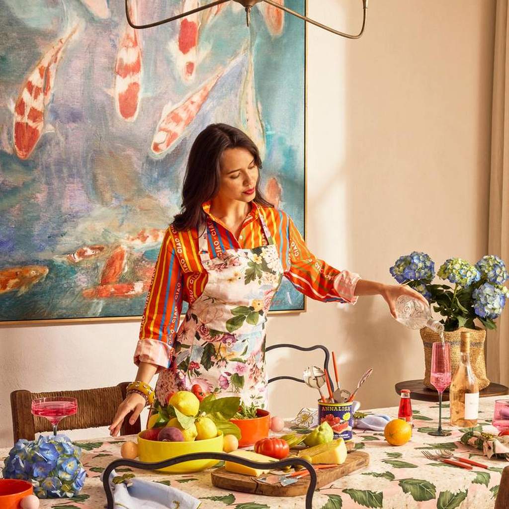 Woman wearing the Belle Floral apron setting a dining table with fruit