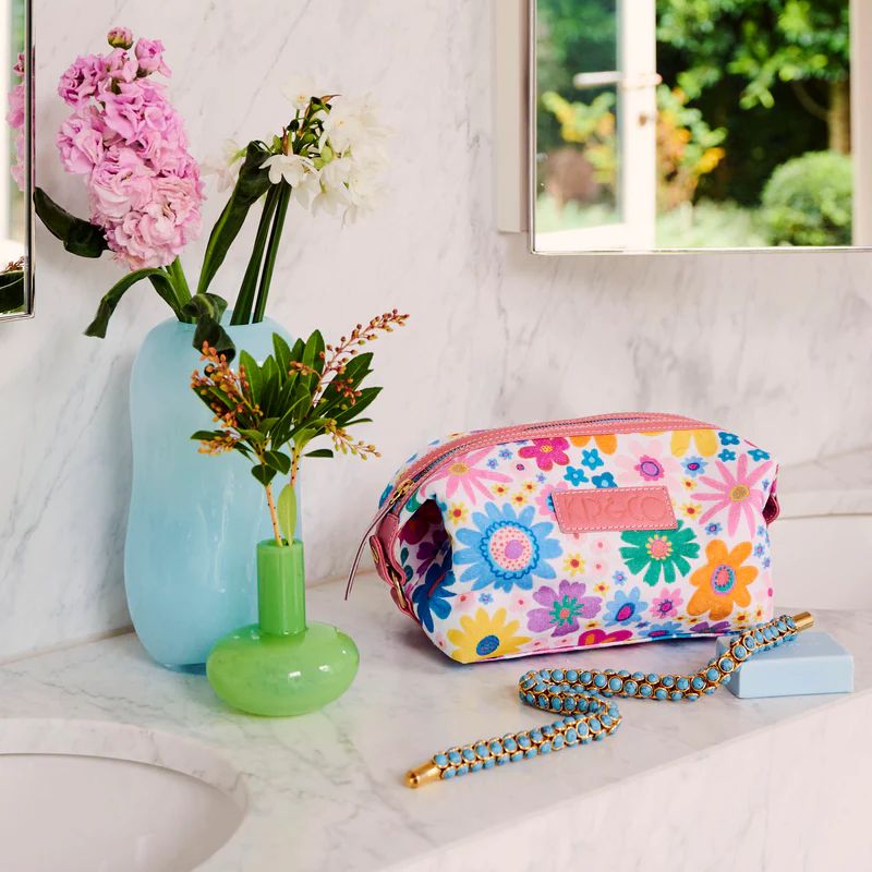 The image likely shows a colorful Kip & Co Rainbow Flowers Toiletry Bag available at Cove. The bag is made from eco-friendly, 100% cotton material, featuring a vibrant floral design.