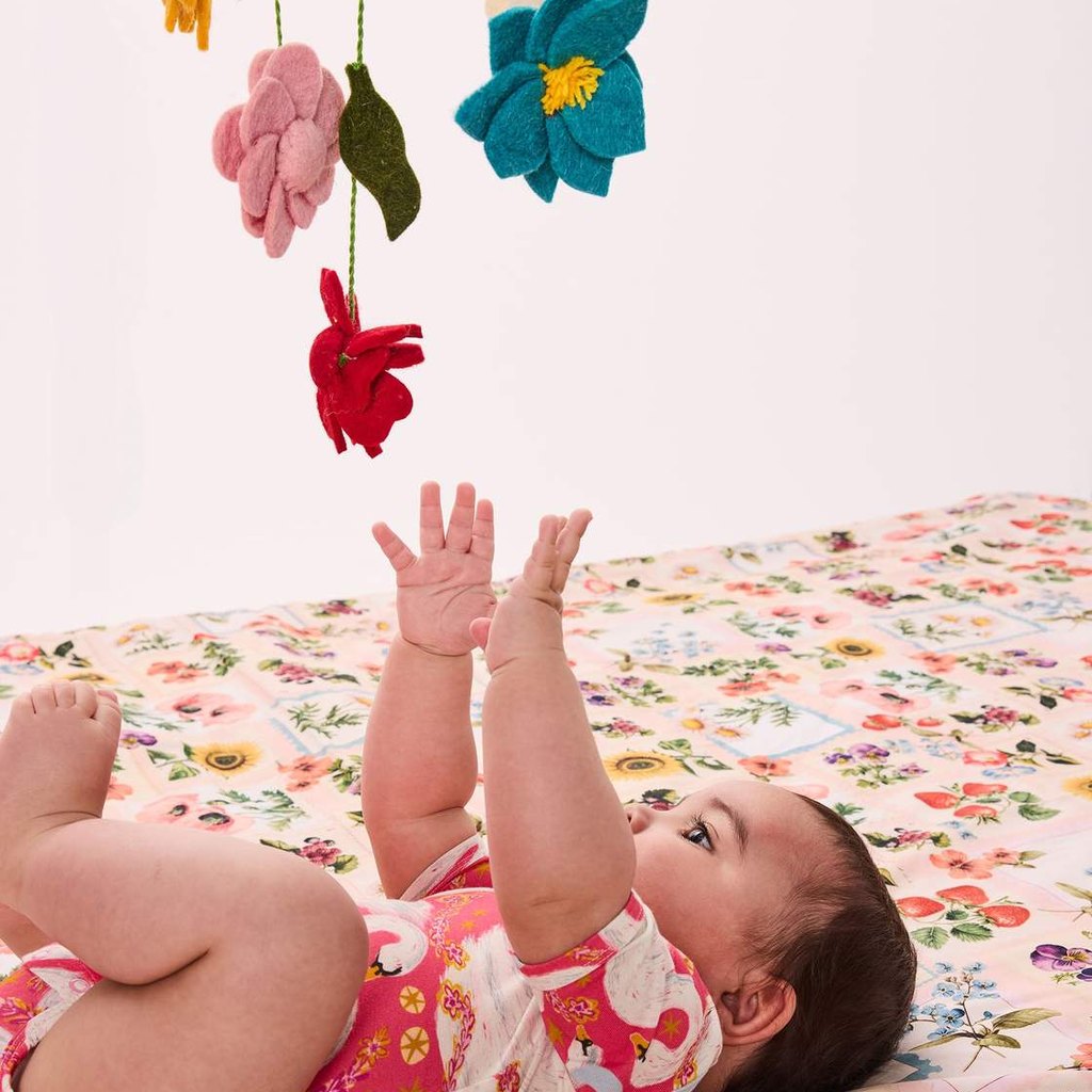 Baby on a floral blanket reaching up to the Little Flowers mobile