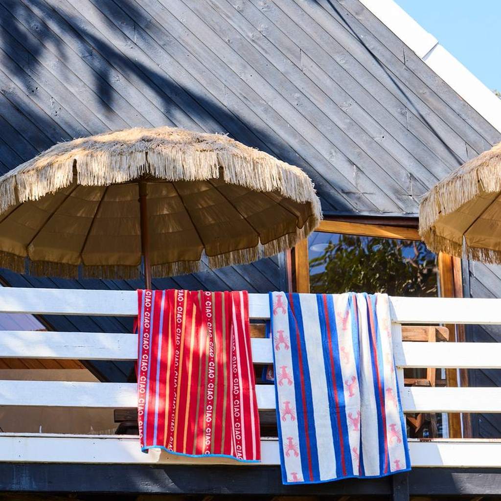 Kip & Co beach towels hanging over a deck rail under a beach umbrella