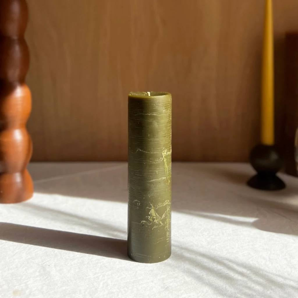 A large olive-colored pillar candle from The Authentic Honey Co., showcasing a smooth, elegant design. The candle is set against a plain background, highlighting its rich hue and substantial size.