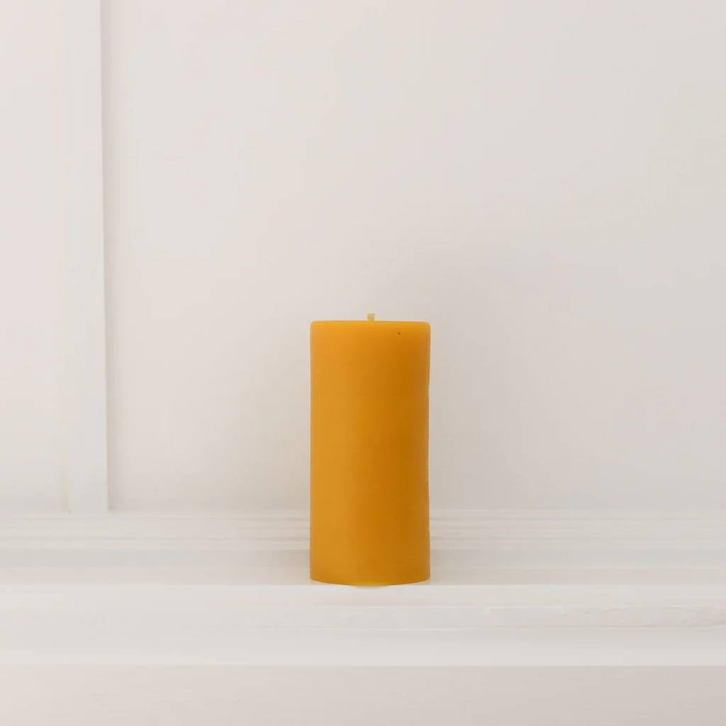 A medium-sized natural beeswax pillar candle from The Authentic Honey Co., showcasing its smooth texture and warm, golden hue. The candle is set against a plain background, highlighting its simple yet elegant design.