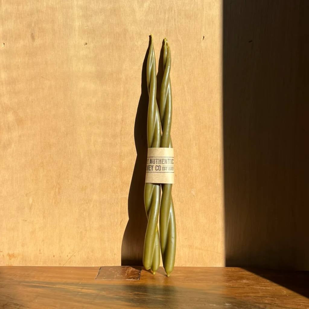 A twisted olive green candle from The Authentic Honey Co. displayed against a plain white background. The candle features a unique spiral design, showcasing its artisanal craftsmanship.