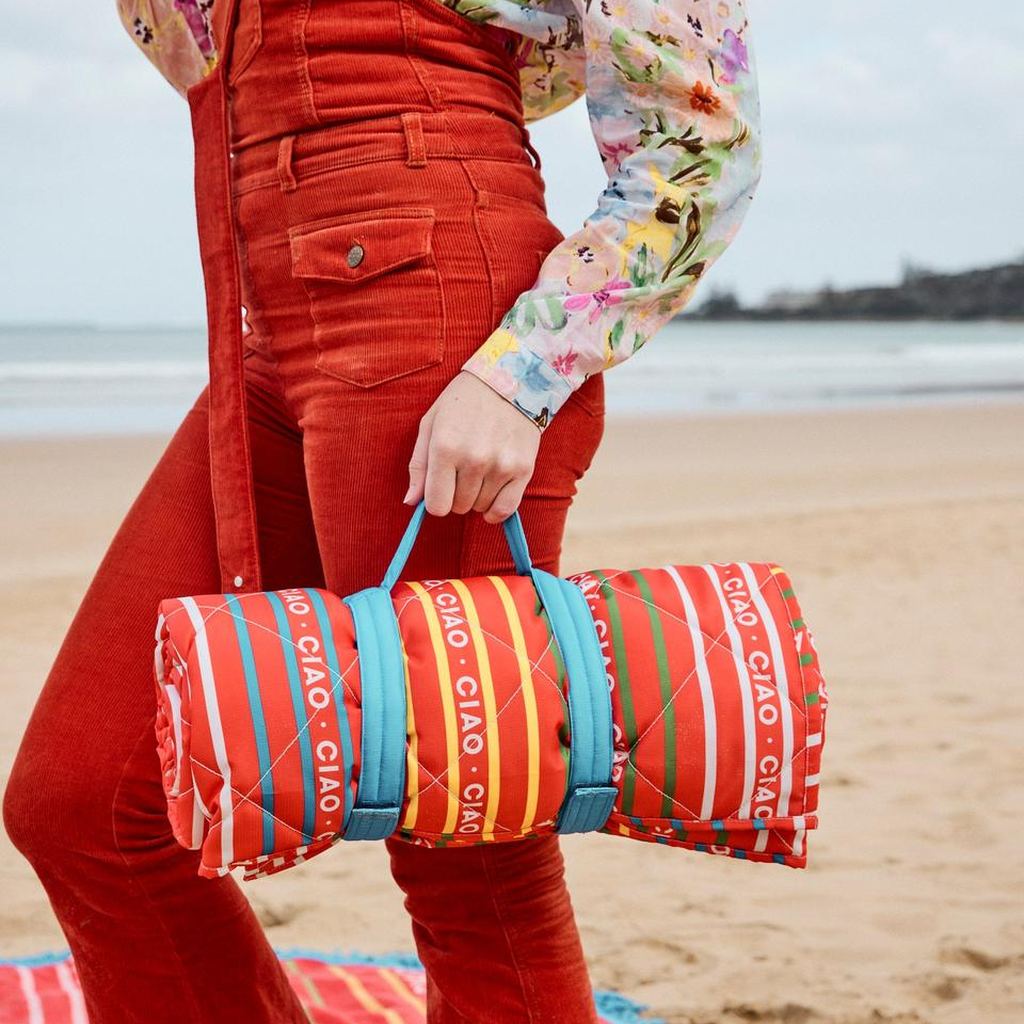 Rolled Ciao Stripe picnic mat carried by the strap