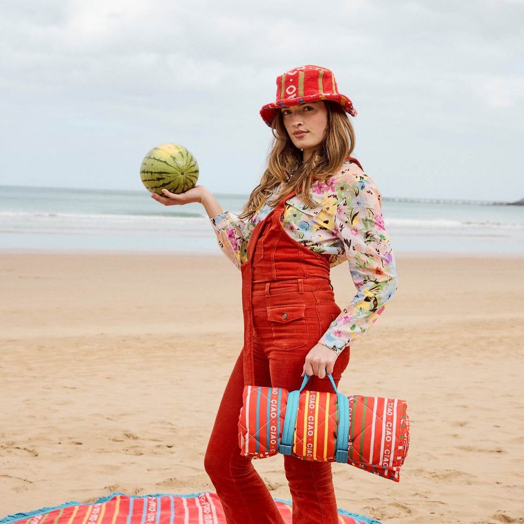 Woman on the beach holding a melon with the rolled Ciao Stripe picnic mat