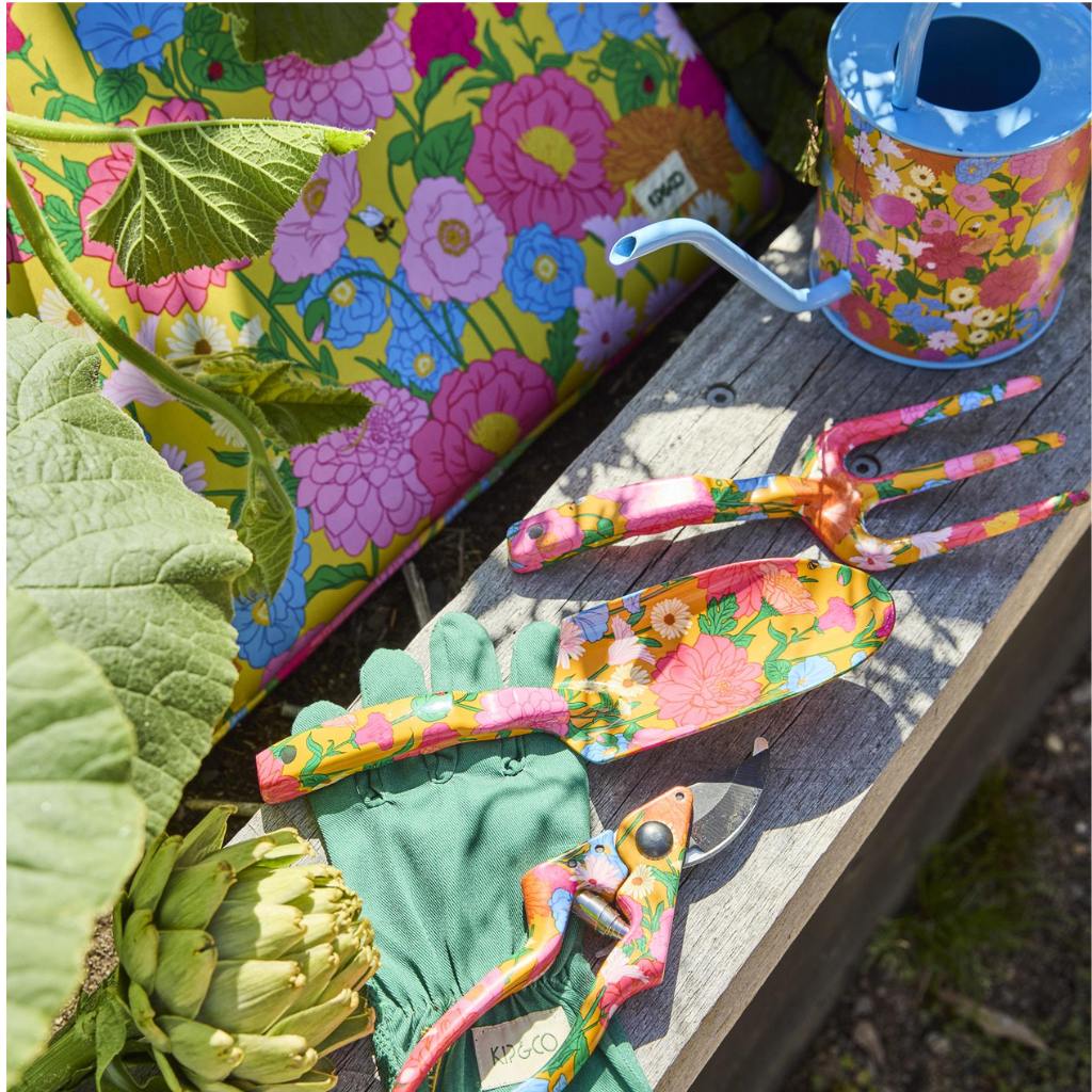 The image is of a garden kneeling mat. It is predominantly yellow with a floral pattern that includes various shades of green, pink, and white. The mat is rectangular with rounded edges and appears to be made of a soft, cushioned material designed to provide comfort while kneeling. The floral design gives it a cheerful and vibrant appearance, suitable for outdoor gardening activities.