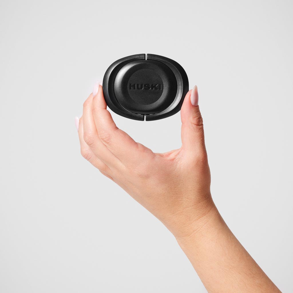 The image shows a Huski BubbleLock Bottle Stopper, a device designed to seal and preserve the contents of a bottle, likely for wine or champagne. The stopper is cylindrical with a sleek, modern design, featuring a metallic finish. The top part of the stopper is slightly wider, with a smooth surface, while the lower part is narrower, designed to fit snugly into the neck of a bottle. The stopper likely uses a locking mechanism to ensure an airtight seal, helping to maintain the freshness and carbonation of th