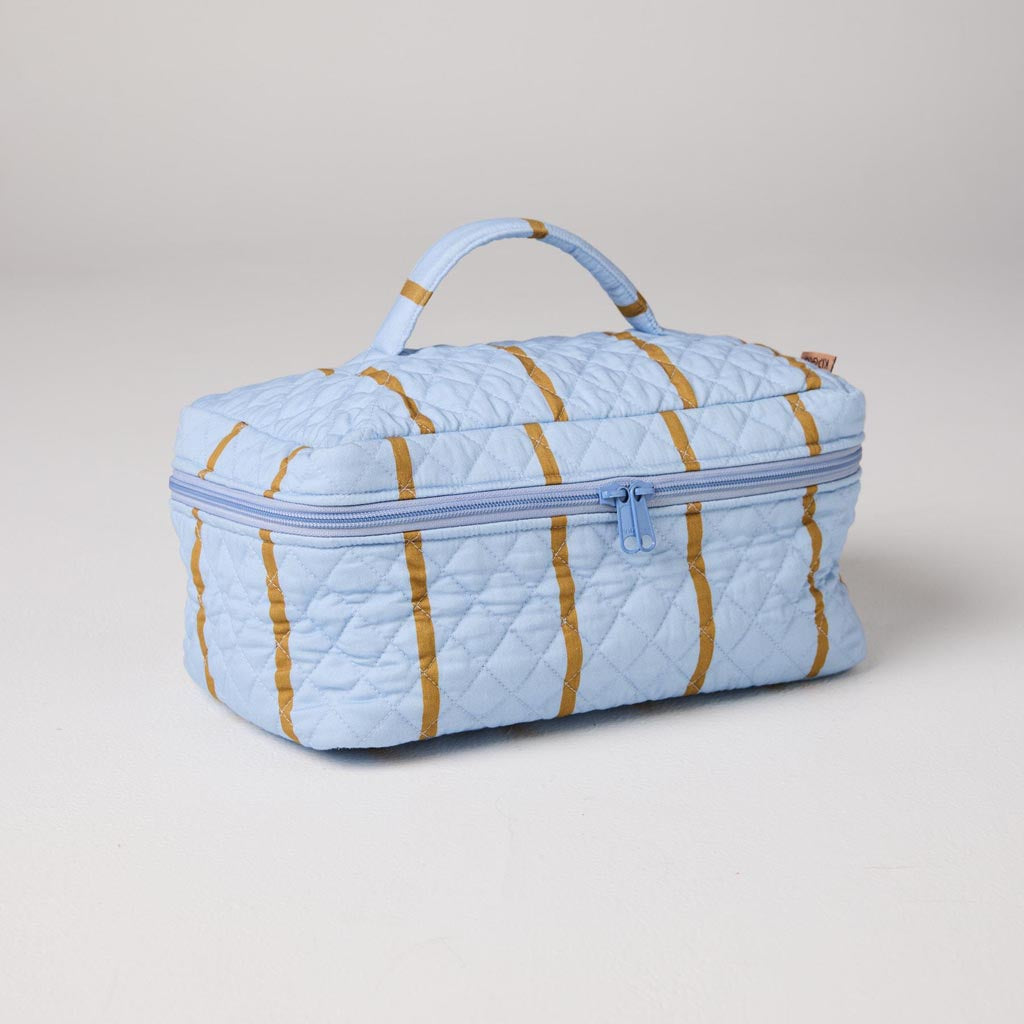 The image shows a quilted cotton toiletry case from Kip & Co, featuring a colorful striped pattern. The stripes are arranged in a variety of colors, including shades of pink, blue, green, and yellow, creating a vibrant and eye-catching design. The case appears to be rectangular in shape with a zipper closure on the top, making it practical for storing toiletries or other small items. The quilted texture adds a touch of softness and dimension to the overall appearance of the case.