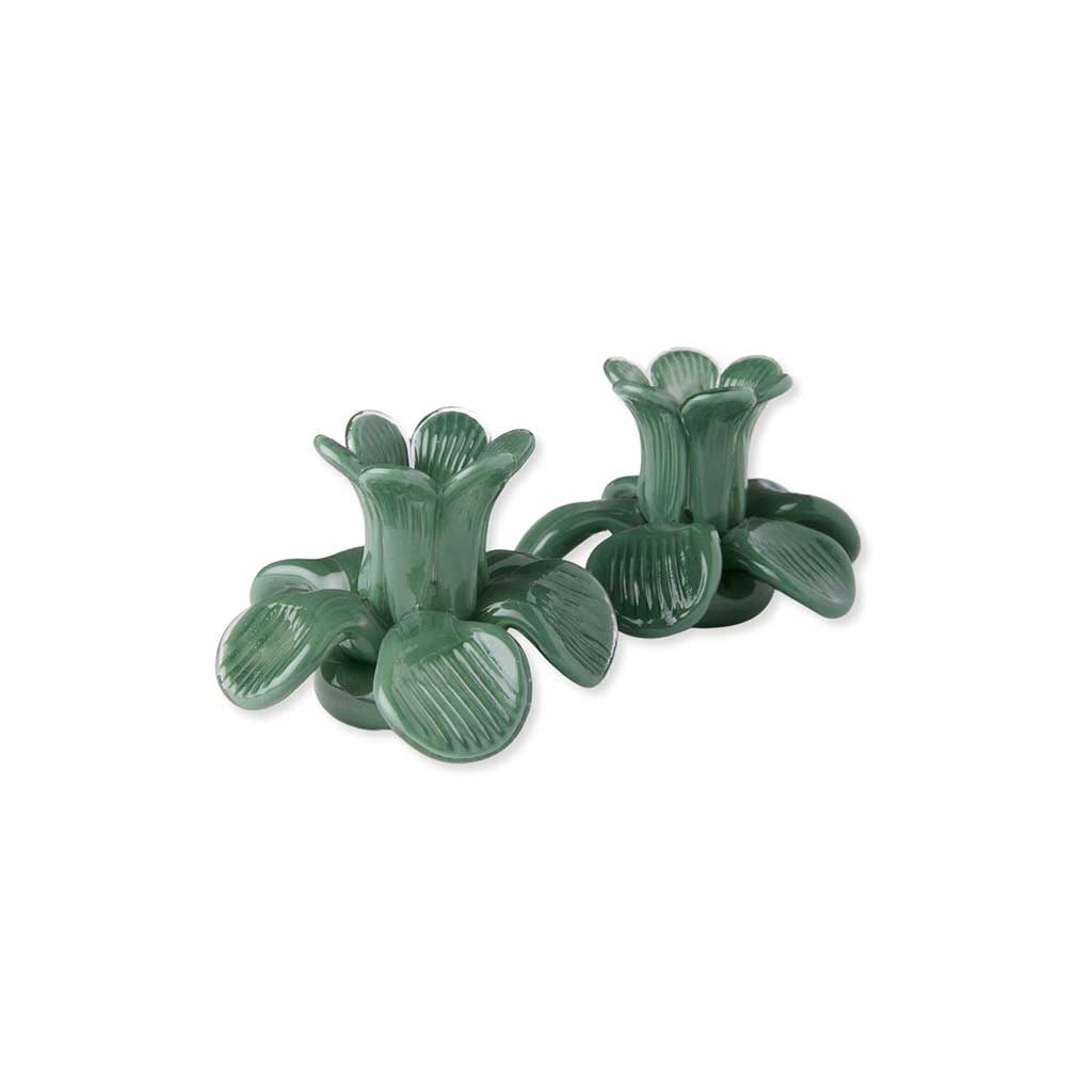The image shows a set of two candle holders designed by Kip & Co. They are shaped like flowers and are colored in a soft pistachio green. Each holder has a central cavity to place a candle, and the petals are intricately designed to resemble a blooming flower. The holders are placed on a plain, neutral background, highlighting their delicate and artistic design.