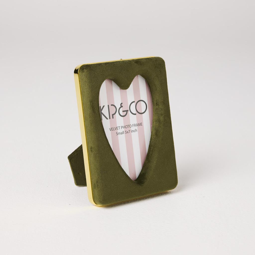 The image is of a photo frame made from velvet material. The frame is designed in a heart shape and features a vibrant, multicolored pattern that resembles a campsite theme. The colors are rich and varied, giving the frame a lively and playful appearance. The frame is intended to hold a 4 x 6-inch photograph, and its unique design makes it a decorative piece suitable for adding a touch of personality to any room.