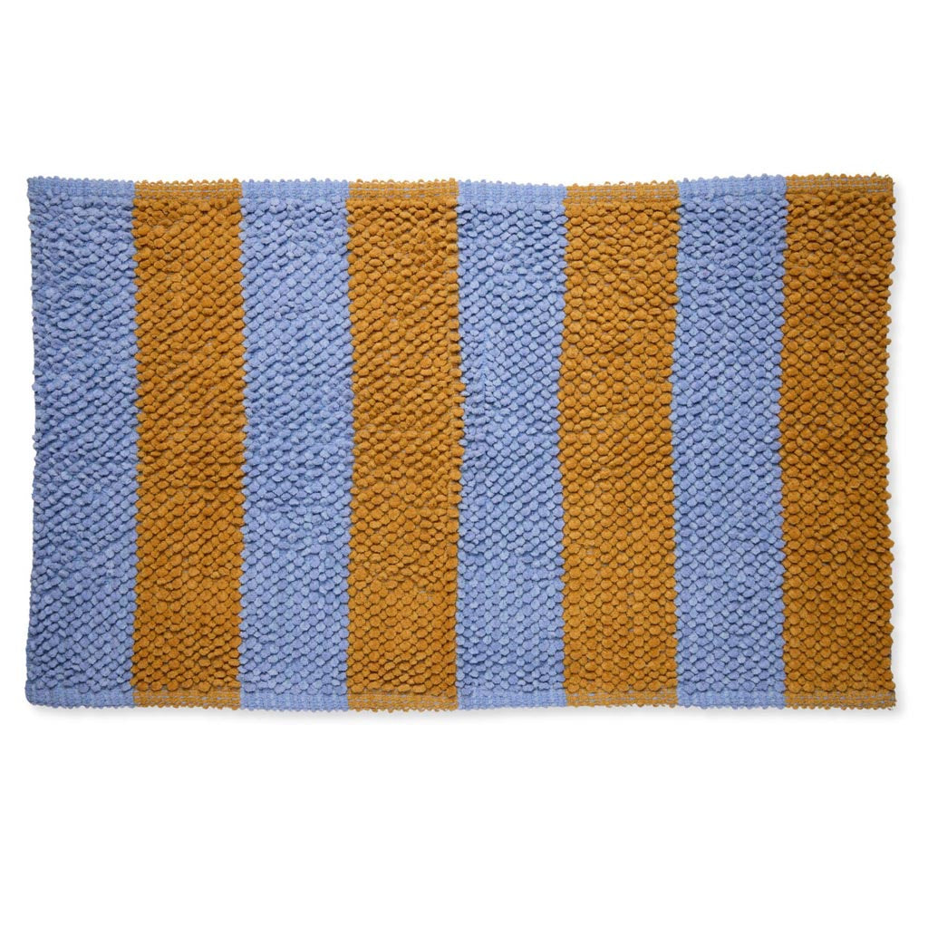 The image is of a colorful bath mat with a striped pattern. The stripes are of varying widths and feature a range of colors, including shades of blue, pink, yellow, and green. The texture of the mat appears soft and plush, suggesting it is made from a comfortable, absorbent material suitable for use in a bathroom setting. The overall design is vibrant and eye-catching, adding a playful touch to bathroom decor.