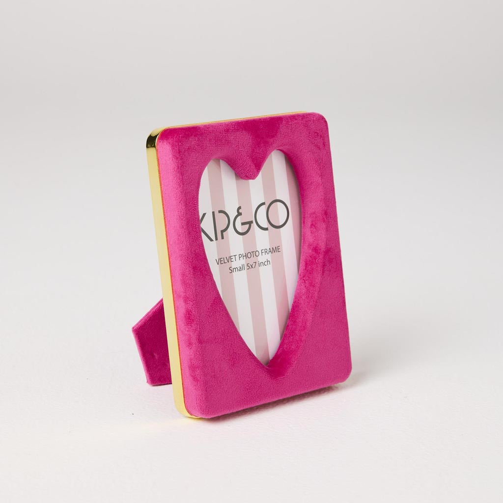 The image is of a photo frame designed by Kip & Co. It features a heart-shaped design and is made from a soft, plush velvet material in a desert pink color. The frame is intended to hold a 6 x 8-inch photograph. The velvet texture gives it a luxurious and cozy appearance, making it a stylish and decorative piece for displaying cherished memories.