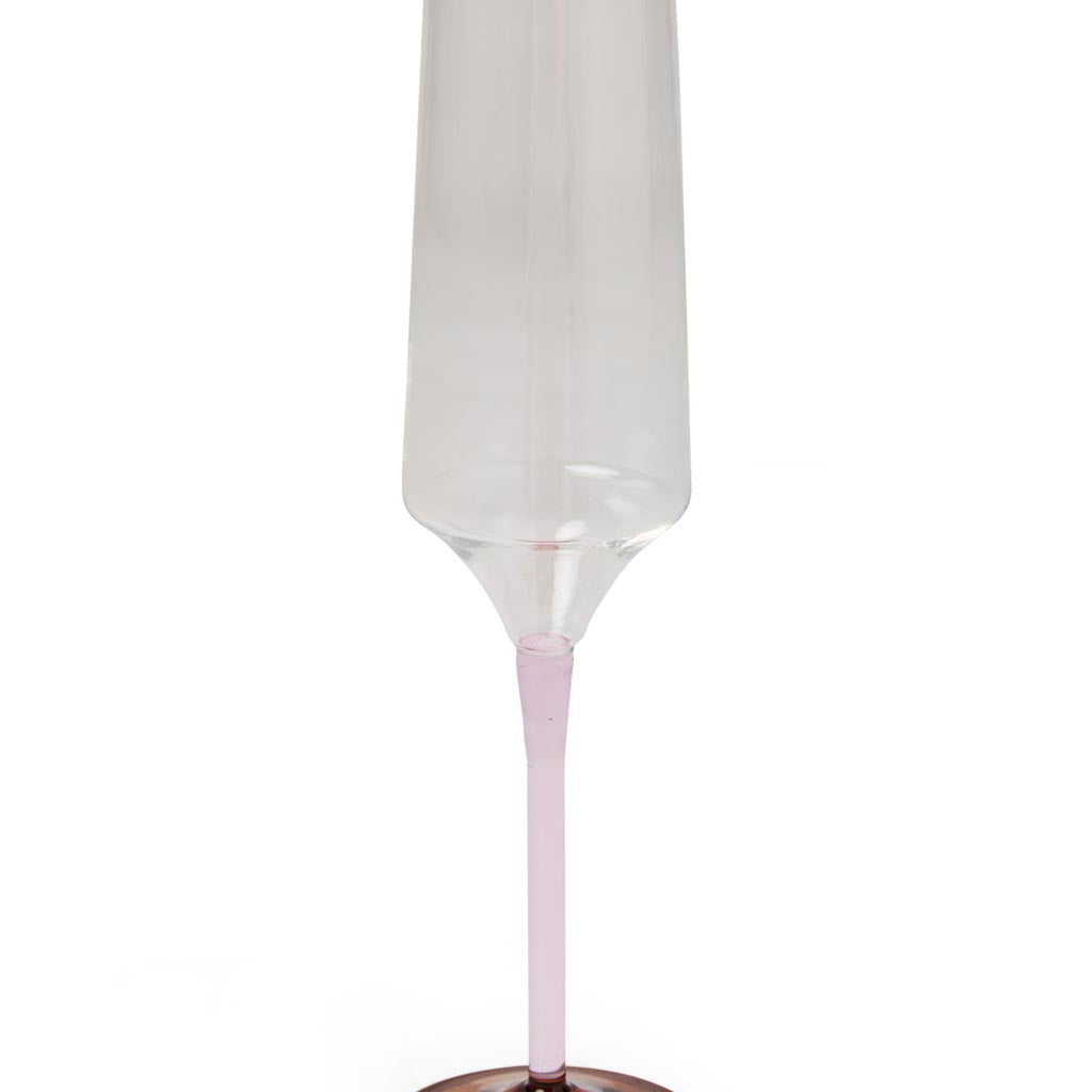 The image shows a set of two champagne glasses from Kip & Co, part of their Marshmallow and Marmalade collection. The glasses are elegantly designed with a delicate, slender stem and a wide, shallow bowl, typical of a coupe-style champagne glass. The glassware features a subtle, colorful gradient that transitions from a soft pink at the base to a warm orange hue towards the rim, reminiscent of a sunset. The glasses are placed against a simple, neutral background, highlighting their vibrant colors and stylis