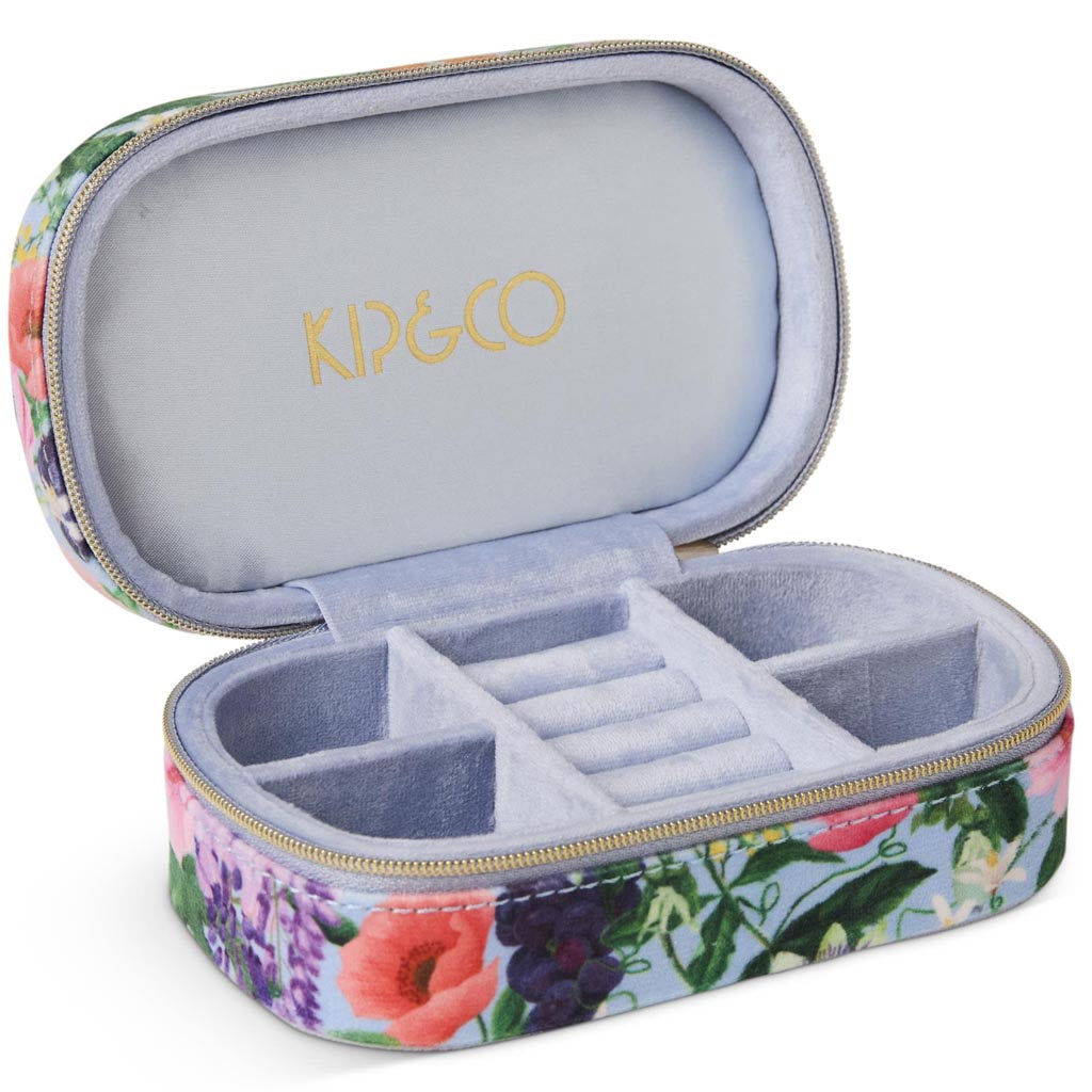 The image shows a small, rectangular velvet jewelry box in a soft pastel pink color. The box has a smooth, plush texture typical of velvet material. It features a gold-colored zipper that runs along the edge, providing a secure closure. The zipper pull is also gold and has a small, elegant design. The box is likely designed for travel, as it is compact and portable, making it convenient for storing and protecting jewelry items while on the go. The background is a simple, neutral color, allowing the jewelry 