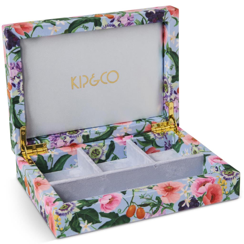 The image shows a small, square-shaped velvet jewelry box. The box is a soft pastel pink color, giving it a delicate and elegant appearance. It features a smooth, plush texture typical of velvet material. The lid of the box is slightly open, revealing a matching pink interior with compartments designed to hold various pieces of jewelry. The overall design is simple yet sophisticated, making it an attractive accessory for storing and organizing jewelry.