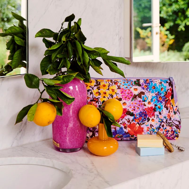 The image shows a Kip &amp; Co Forever Floral Lilac Purse, featuring a vibrant floral pattern in shades of lilac and other complementary colors. The purse is designed to be both stylish and eco-friendly, offering ample space for essentials.