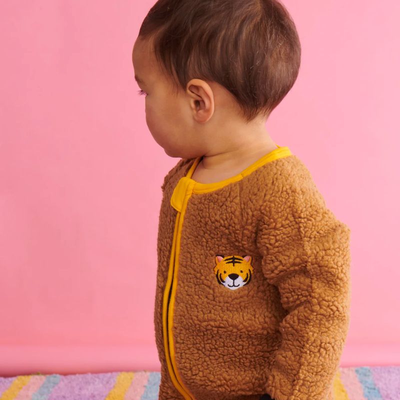 The image shows a cozy and adorable baby romper from Kip & Co, known as the Little Tiger Sherpa Romper. The romper features a playful tiger print and is made from eco-friendly materials, perfect for keeping your baby warm and snug.