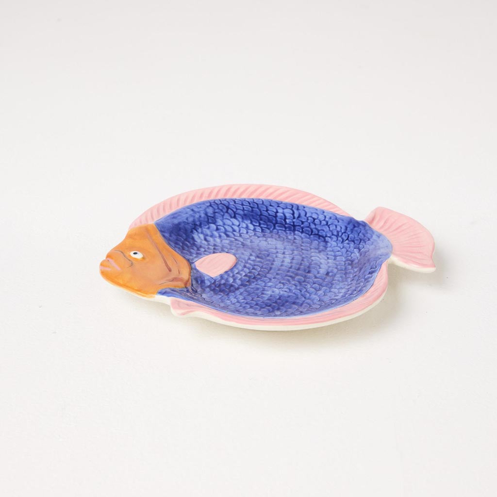 The image is of a colorful, fish-shaped serving dish. The dish is designed to resemble a fish, with a detailed depiction of scales, fins, and a tail. The colors are vibrant, featuring a mix of blues, greens, and yellows, giving it a tropical and lively appearance. The dish is likely made of ceramic or a similar material, and it is intended for serving food, possibly as a decorative piece for a dining table or kitchen.