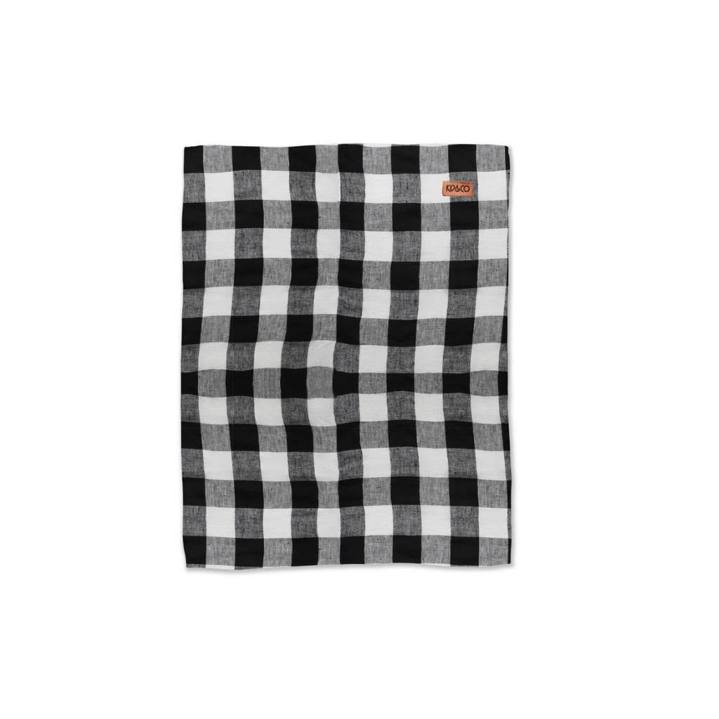 The image likely showcases Kip & Co's Gingham Linen Tea Towel, highlighting its design and texture. The towel is displayed in a kitchen setting, emphasizing its eco-friendly nature and stylish addition to home decor.