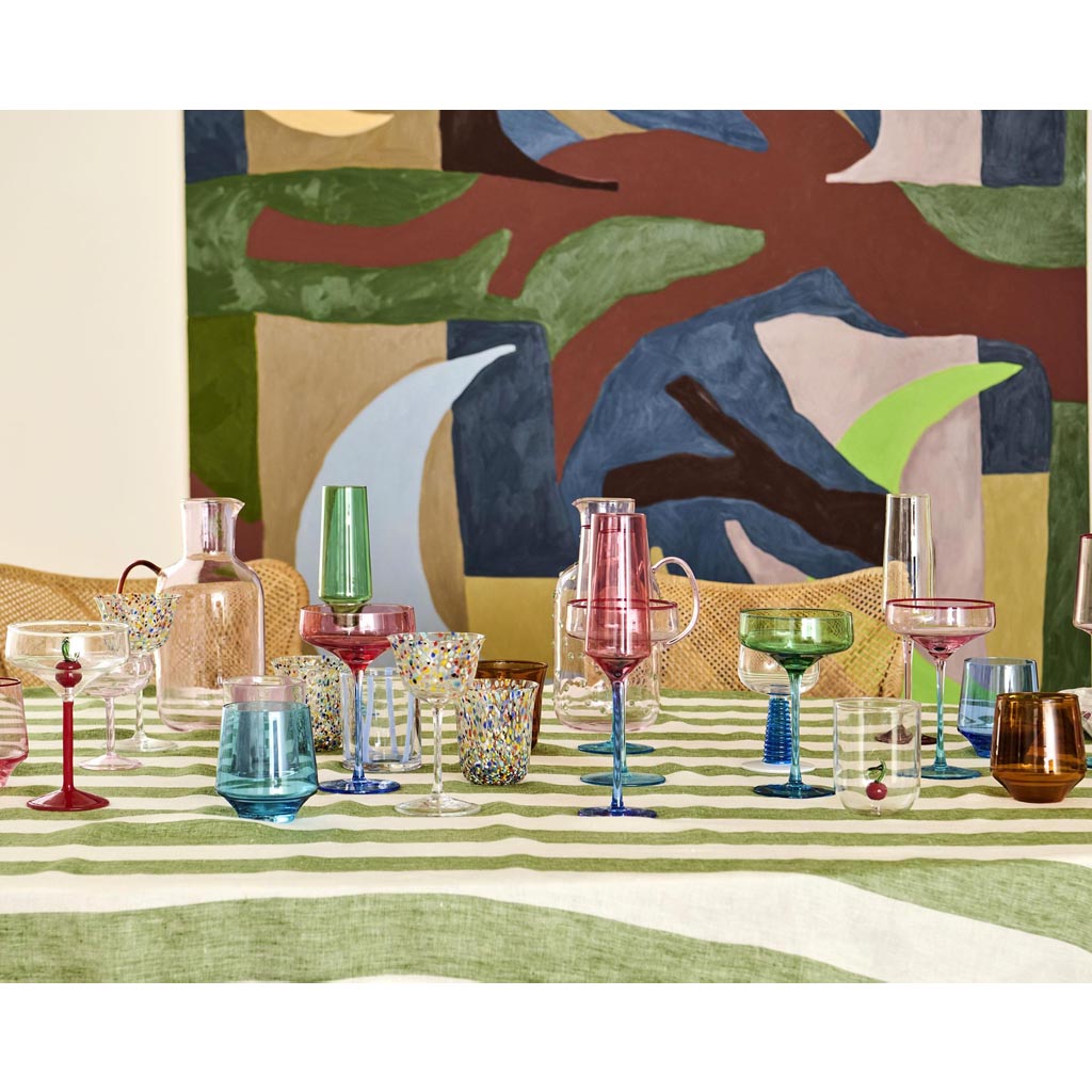 The image shows a set of four champagne glasses, each with a unique and colorful design. The glasses are arranged in a neat row, showcasing their vibrant patterns. The designs feature a mix of blue, green, and other bright colors, resembling abstract or artistic motifs. The glasses have a slender stem and a wide, shallow bowl typical of champagne glasses. They are set against a plain, neutral background, which highlights their colorful appearance.