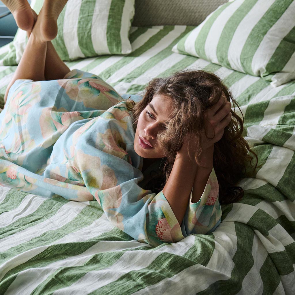 The image shows a blue linen robe with a vibrant floral pattern. The robe features a mix of large, colorful flowers in shades of pink, orange, and yellow, set against a blue background. The robe has a relaxed fit with long sleeves and a belt for tying at the waist. The fabric appears lightweight and comfortable, suitable for lounging or casual wear. The overall design is bold and eye-catching, combining elegance with a touch of whimsy.