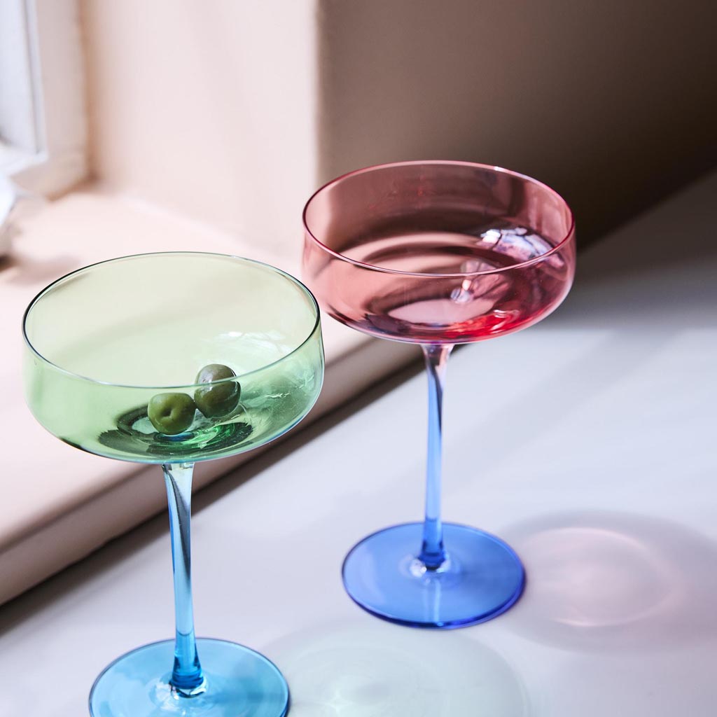 The image shows a set of two margarita glasses from Kip & Co. Each glass features a unique design with a blue robin motif. The glasses are elegantly shaped with a wide, shallow bowl and a sturdy stem, typical of margarita glasses. The blue robin design adds a touch of whimsy and color, making these glasses both functional and decorative. They are likely displayed on a neutral background to highlight their intricate design and vibrant colors.