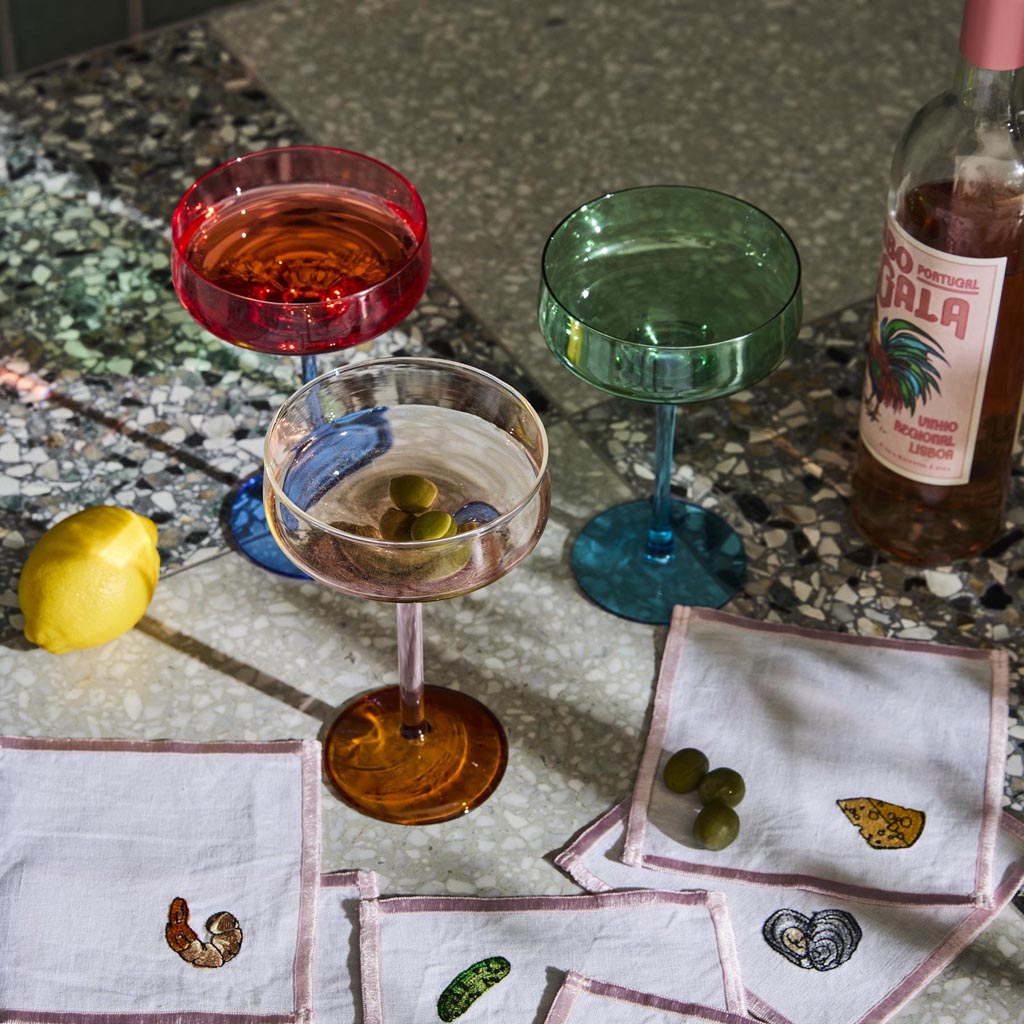 The image shows a set of two margarita glasses from Kip & Co. Each glass features a unique design with a blue robin motif. The glasses are elegantly shaped with a wide, shallow bowl and a slender stem, typical of margarita glassware. The blue robin design adds a touch of whimsy and color, making the set both functional and decorative. The glasses are placed against a plain background, highlighting their intricate design and craftsmanship.