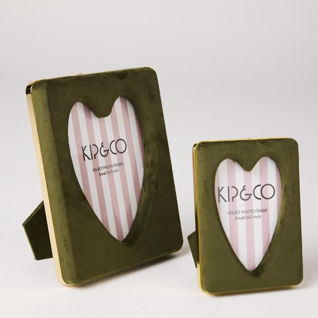 The image is of a photo frame designed by Kip & Co, known as the Campsite Heart Velvet Photo Frame. The frame is made from a plush velvet material, giving it a soft and luxurious appearance. It is shaped like a heart, adding a whimsical and romantic touch. The frame is designed to hold a photo measuring 4 x 6 inches. The velvet fabric is likely in a vibrant or rich color, typical of Kip & Co's bold and playful design aesthetic. The overall look is both stylish and cozy, making it a charming addition to any 