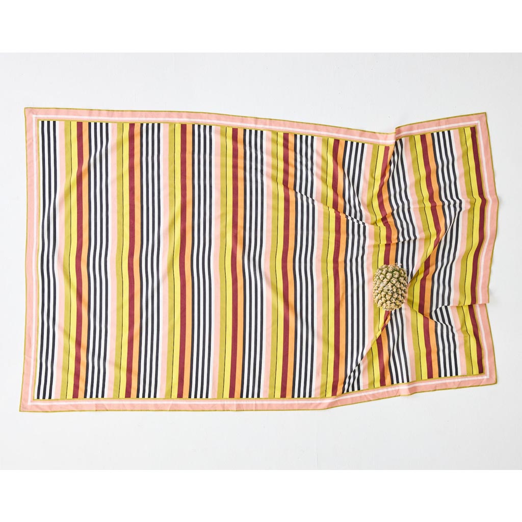 The image shows a colorful striped sarong made from organic cotton. The sarong features a pattern of horizontal stripes in various vibrant colors, including shades of pink, orange, yellow, green, and blue. The fabric appears lightweight and soft, suitable for use as a beach cover-up or a versatile accessory. The background is plain, allowing the colors and texture of the sarong to stand out prominently.