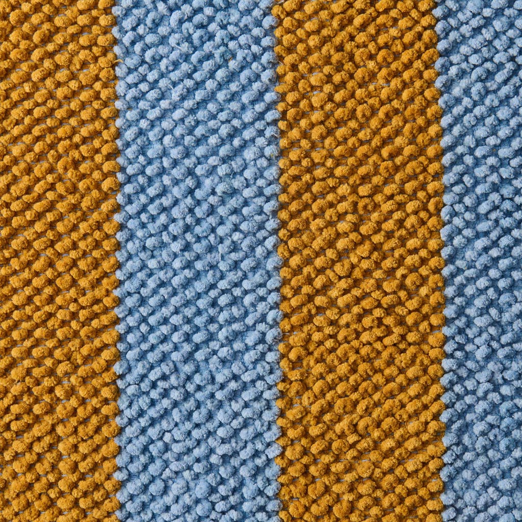 The image shows a colorful bath mat with a striped pattern. The stripes are arranged in a horizontal fashion and feature a variety of vibrant colors, including shades of pink, orange, yellow, green, blue, and purple. The texture of the mat appears soft and plush, suggesting it is made from a comfortable, absorbent material suitable for use in a bathroom setting. The overall design is lively and eye-catching, adding a pop of color to any bathroom decor.