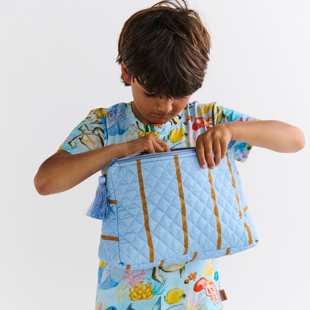 The image is of a quilted cotton toiletry purse from Kip & Co, featuring a colorful striped pattern called "Como Stripe." The purse has a rectangular shape with a zipper closure at the top. The stripes are in various vibrant colors, creating a lively and eye-catching design. The quilted texture adds a layer of dimension and softness to the purse. The background of the image is plain, allowing the purse to be the focal point.