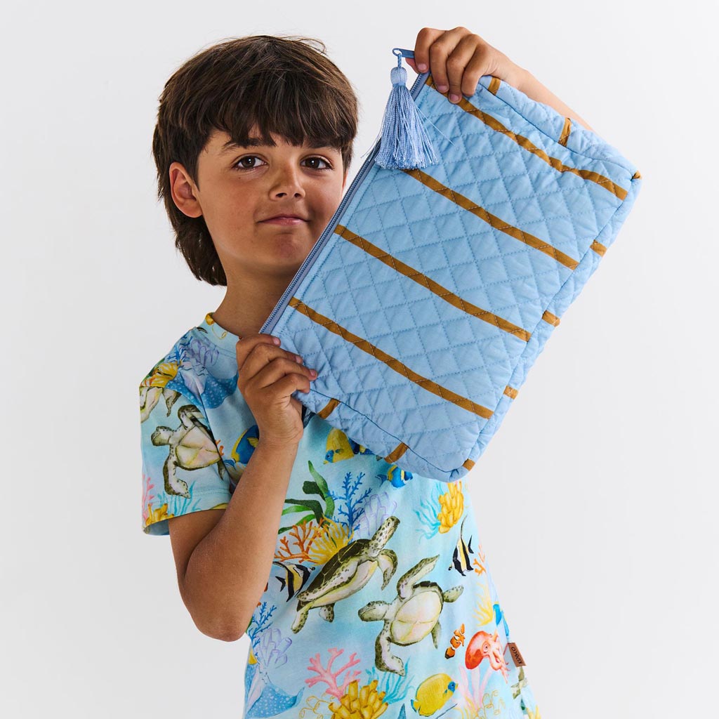 The image is of a quilted cotton toiletry purse from Kip & Co, featuring a colorful striped pattern called "Como Stripe." The purse has a rectangular shape with a zipper closure at the top. The stripes are in various vibrant colors, creating a lively and eye-catching design. The quilted texture adds a layer of dimension and softness to the purse. The background of the image is plain, allowing the purse to be the focal point.