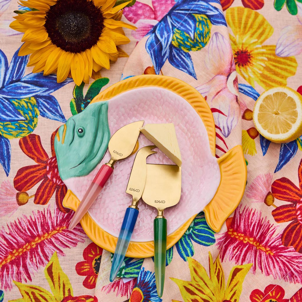 The image shows a decorative serving dish shaped like a fish. The dish is designed with vibrant colors and intricate patterns, resembling coral reefs and oceanic themes. The body of the fish is adorned with a mix of blues, greens, and coral hues, giving it a lively and artistic appearance. The dish is likely made of ceramic or a similar material, and it is intended for serving food, adding a touch of whimsy and elegance to dining settings.