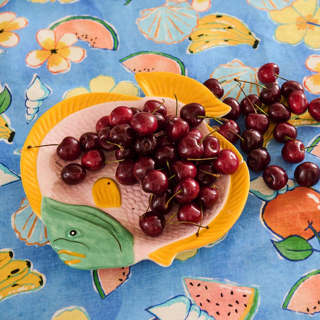 The image shows a decorative serving dish designed in the shape of a fish. The dish features a vibrant and colorful pattern, with a mix of coral, pink, and blue hues, reminiscent of a coral reef or oceanic theme. The intricate design includes various abstract shapes and lines, giving it an artistic and lively appearance. The dish is likely made of ceramic or a similar material, and it is placed on a plain background to highlight its unique design.
