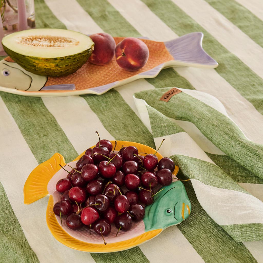 The image is of a decorative serving dish designed in the shape of a fish. The dish features a vibrant and colorful pattern, with a mix of coral, pink, and blue hues that resemble the scales and natural patterns found on a fish. The design is artistic and whimsical, making it an eye-catching piece for serving food or as a decorative item in a home setting. The dish appears to be made of ceramic or a similar material, giving it a glossy finish.