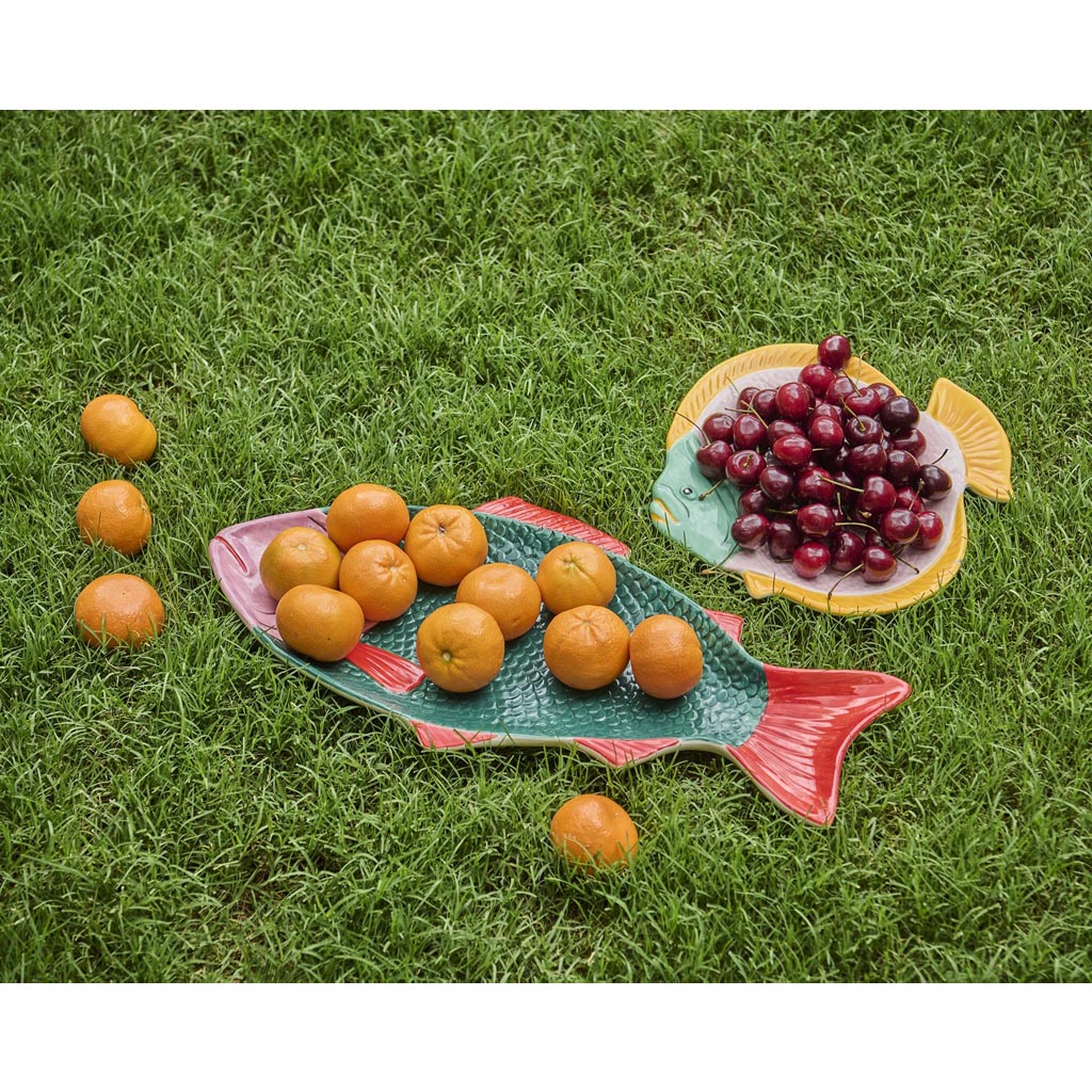 The image is of a decorative serving dish shaped like a fish. The dish features a vibrant and colorful design, with a mix of coral, pink, and blue hues. The fish's scales are intricately detailed, and the overall appearance is both artistic and functional, making it suitable for serving food or as a decorative piece. The dish is set against a plain background, highlighting its unique design and colors.