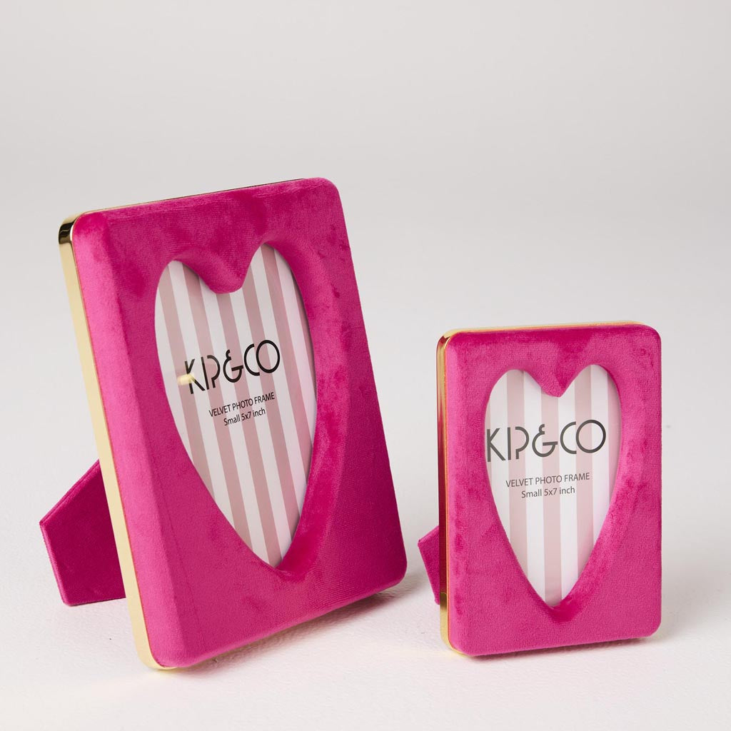 The image is of a photo frame designed by Kip & Co. It features a heart-shaped design and is made from a soft, plush velvet material in a desert pink color. The frame is intended to hold a 6 x 8-inch photograph. The velvet texture gives it a luxurious and cozy appearance, making it a stylish and decorative piece for displaying cherished memories.