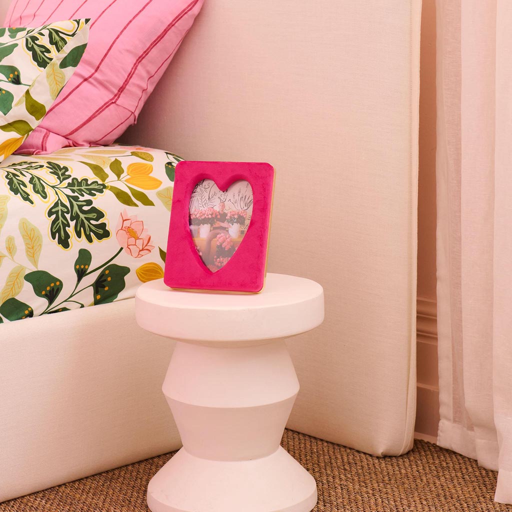 The image is of a photo frame designed by Kip & Co. It features a heart-shaped design and is made from a soft, plush velvet material in a desert pink color. The frame is intended to hold a 6 x 8-inch photograph. The velvet texture gives it a luxurious and cozy appearance, making it a stylish and decorative piece for displaying cherished memories.