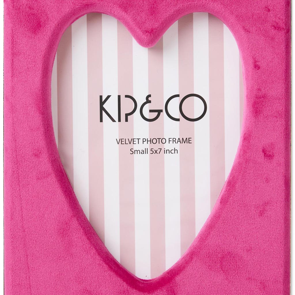 The image is of a photo frame designed by Kip & Co. It features a heart-shaped design and is made from a soft, desert pink velvet material. The frame is intended to hold a 6 x 8 inch photograph. The velvet texture gives it a luxurious and plush appearance, and the pink color adds a warm, inviting feel. The heart shape makes it ideal for displaying cherished memories or as a decorative piece in a room.