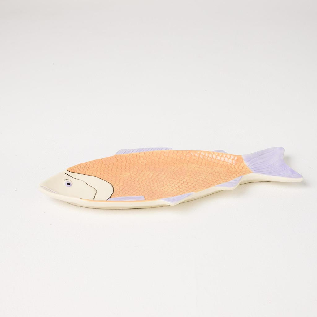 The image is of a decorative serving dish shaped like a fish. The dish is likely made of ceramic or a similar material and features a colorful design with intricate patterns. The body of the fish is adorned with vibrant hues, possibly including shades of blue, green, and other complementary colors, giving it a lively and artistic appearance. The dish is designed to be both functional and visually appealing, suitable for serving food or as a decorative piece in a dining setting.