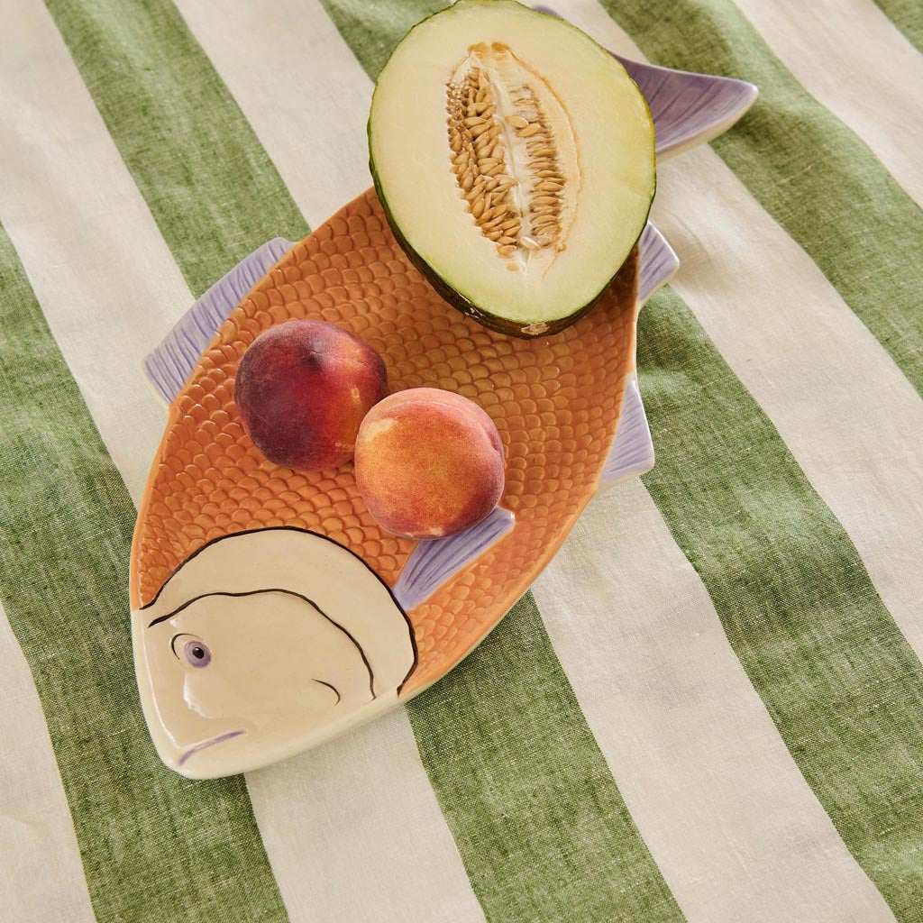 The image shows a decorative serving dish shaped like a fish. The dish is likely made of ceramic or a similar material and features a colorful, intricate design. The body of the fish is adorned with vibrant patterns and hues, possibly inspired by tropical or oceanic themes. The dish is designed to be both functional and aesthetically pleasing, suitable for serving food or as a decorative piece in a home setting.