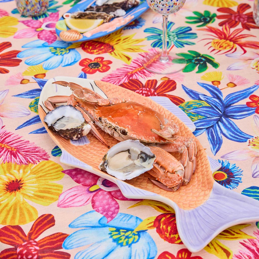 The image shows a decorative serving dish shaped like a fish. The dish is likely made of ceramic or a similar material and features a colorful, intricate design. The body of the fish is adorned with vibrant patterns and hues, possibly inspired by tropical or oceanic themes, giving it an artistic and lively appearance. The dish is designed to be both functional and visually appealing, suitable for serving food or as a decorative piece in a home setting.