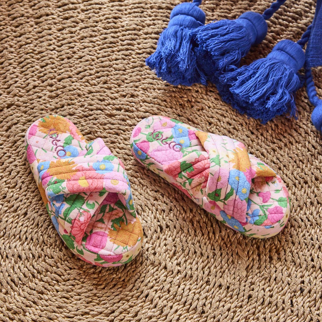 The image shows a pair of adult slippers made from quilted velvet material. The slippers are designed with a soft, plush texture and feature a vibrant, multicolored pattern. The colors include shades of pink, orange, yellow, and blue, arranged in a way that resembles a patchwork or mosaic design. The slippers have a closed-toe style and appear to be cozy and comfortable, suitable for indoor wear. They are displayed against a plain background, highlighting their colorful and luxurious appearance.