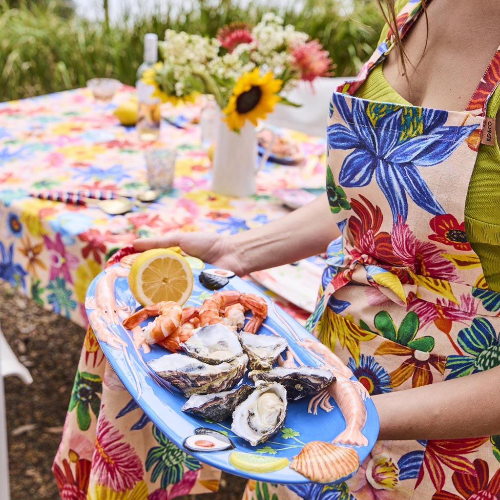 The image is of a large oval platter from Kip & Co, featuring a vibrant and colorful design. The platter is adorned with an artistic depiction of various sea creatures and marine elements, such as fish, shells, and seaweed, all rendered in a playful and whimsical style. The colors are bright and eye-catching, with a mix of blues, greens, pinks, and yellows, creating a lively and cheerful appearance. The platter's design is likely intended to evoke a sense of the ocean and marine life, making it a striking p