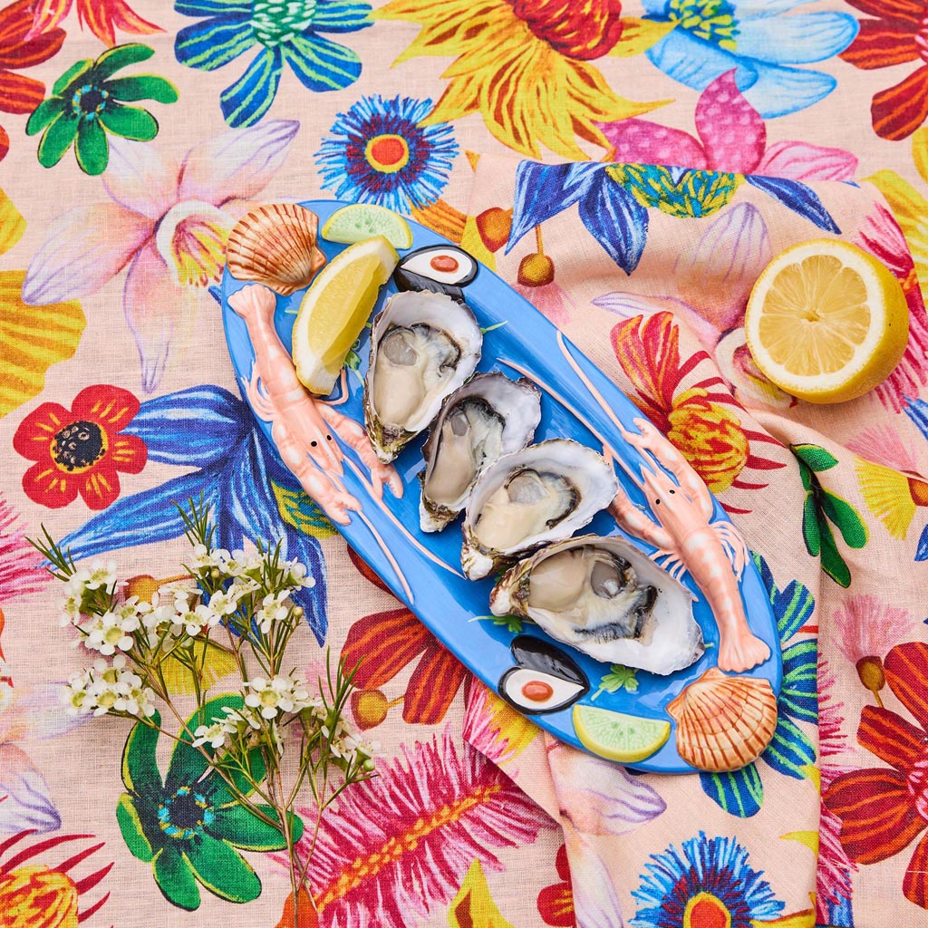 The image is of a small oval platter from Kip & Co, featuring a vibrant and colorful design. The platter is adorned with an artistic depiction of various sea creatures and marine elements, such as fish, shells, and seaweed, in a playful and whimsical style. The colors are bright and eye-catching, with a mix of blues, greens, pinks, and yellows, creating a lively and cheerful appearance. The platter's design is likely intended to evoke a sense of the ocean and marine life, making it a decorative and function