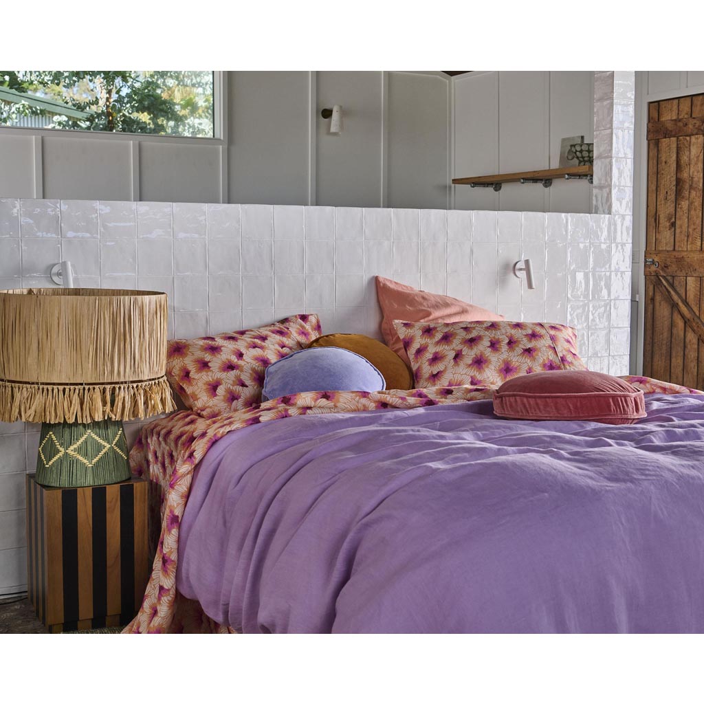 The image shows a stylish table lamp with a unique design. The lamp features a base made of natural raffia material, giving it a textured and organic appearance. The lampshade is likely made of a similar material or a complementary fabric, contributing to a cohesive and earthy aesthetic. The overall look of the lamp is modern yet rustic, making it a versatile piece for various interior design styles. The background is plain, ensuring the focus remains on the lamp itself.