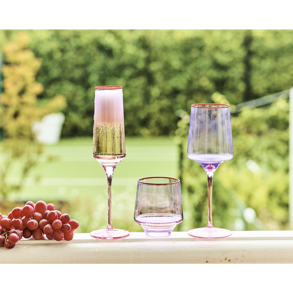 The image shows a pair of elegant wine glasses with a unique color block design. The glasses have a lilac hue at the base, transitioning into a clear glass towards the top. They are set against a plain background, highlighting their modern and artistic design. The glasses appear to be part of a stylish and contemporary collection, suitable for adding a pop of color to any table setting.