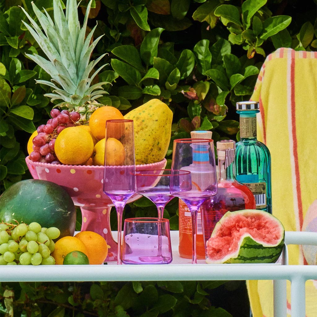 The image features a pair of elegant wine glasses with a unique color block design. Each glass has a stem and base in a soft lilac hue, while the bowl of the glass is clear, allowing the wine inside to be visible. The glasses are set against a plain white background, highlighting their modern and stylish appearance. The design is simple yet sophisticated, making these glasses suitable for both casual and formal settings.