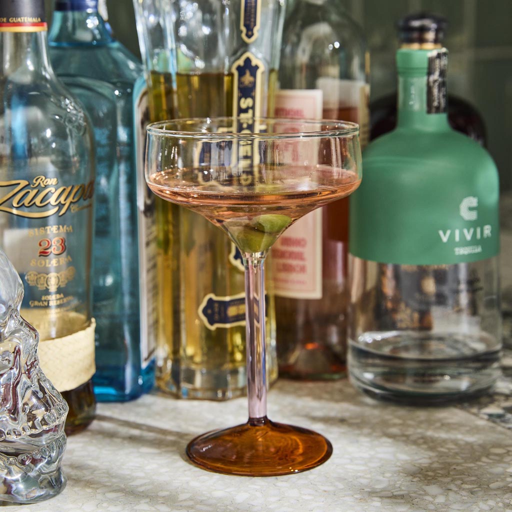 The image shows a set of two margarita glasses from Kip & Co. Each glass features a unique and colorful design, with a combination of pastel and vibrant hues resembling marshmallows and marmalade. The glasses have a classic margarita shape with a wide, shallow bowl and a long stem, making them both stylish and functional for serving cocktails. The background is plain, allowing the intricate patterns and colors of the glasses to stand out.