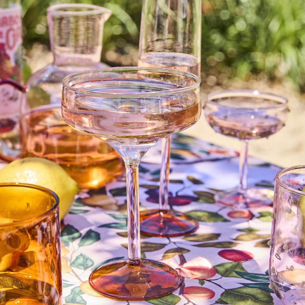 The image shows a set of two margarita glasses from Kip & Co. Each glass features a unique and colorful design, with a combination of pastel and vibrant hues resembling marshmallows and marmalade. The glasses have a classic margarita shape with a wide, shallow bowl and a short stem. The artistic design on the glasses adds a playful and whimsical touch, making them stand out as decorative and functional pieces for serving drinks. The background is plain, highlighting the intricate details and colors of the g